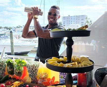 ISLE Bartend mixologist Tony shaking a cocktail above a tiered fresh fruit display at a waterfront marina